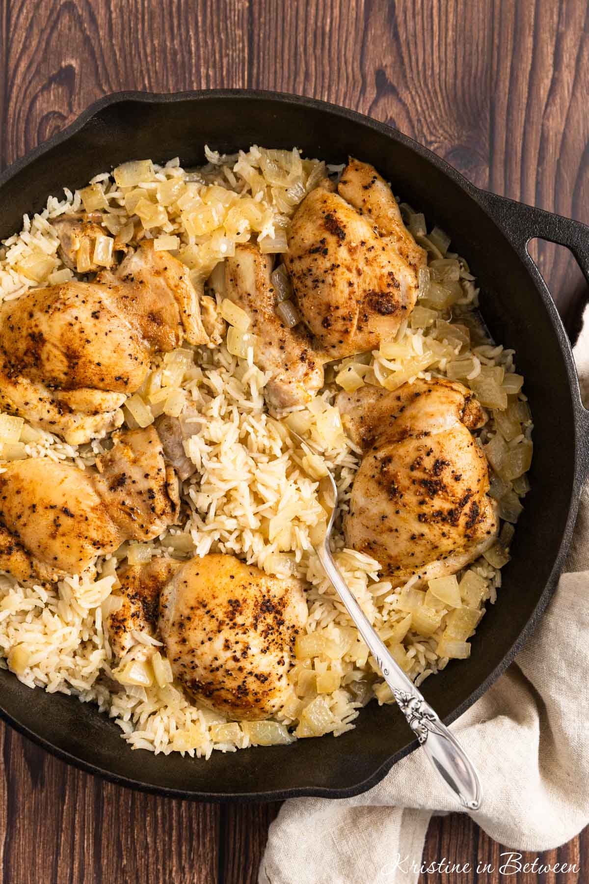 Cooked chicken thighs and right in a cast iron pan with a spoon.