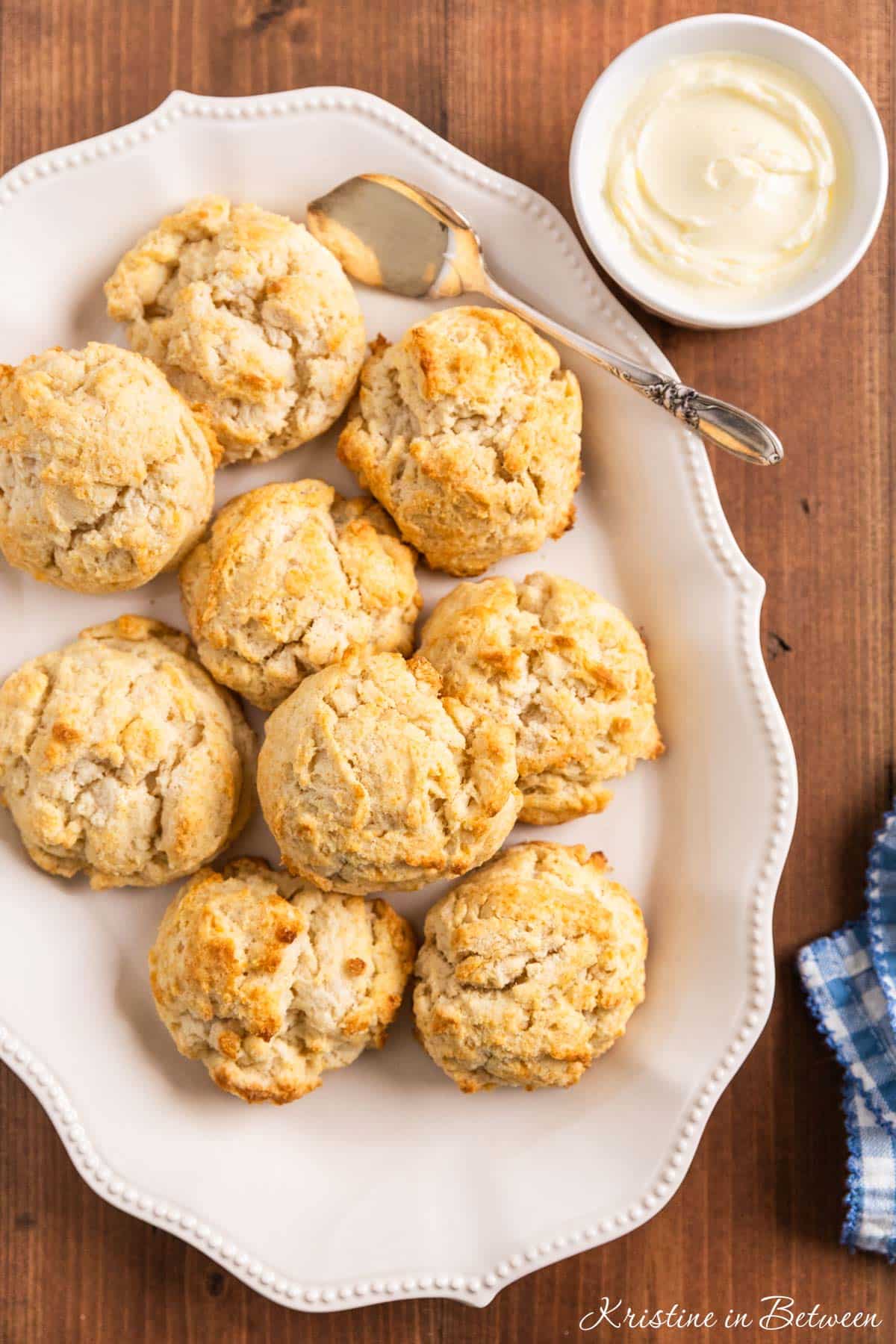 A pate of homemade drop biscuits sitting with an antique spreader and a small bowl of butter.
