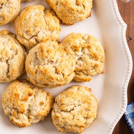 Old-fashioned drop biscuits stacked up on a white platter with a butter knife.