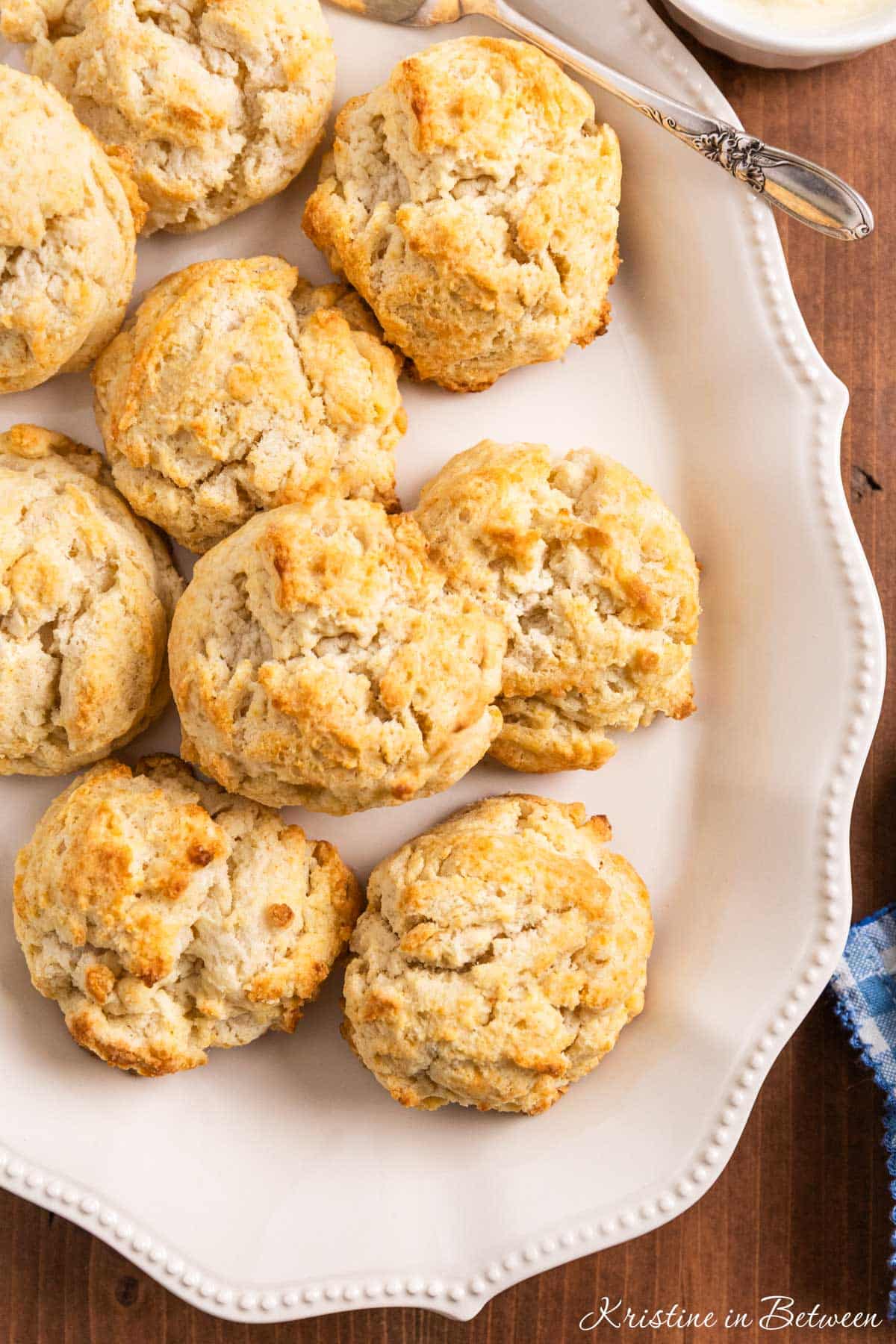 Old-fashioned drop biscuits stacked up on a white platter with a butter knife.