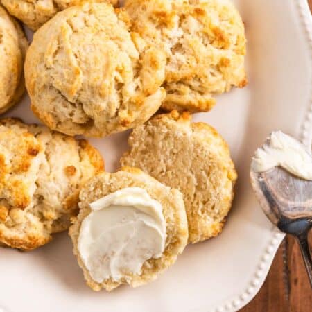 Homemade biscuits on a plate with one cut in half and lightly buttered.
