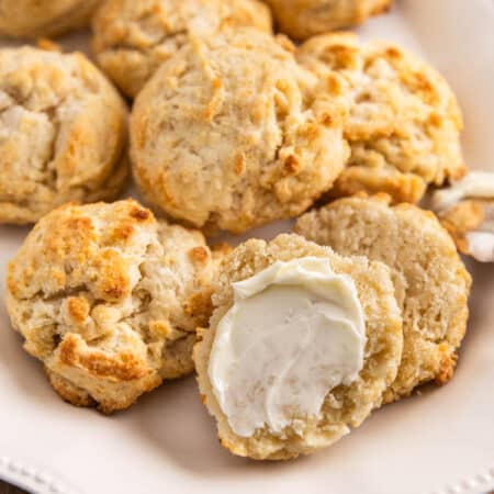 Homemade biscuits on a plate with one cut in half and lightly buttered.
