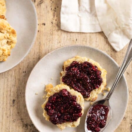 A biscuit cut in half with raspberry chia seed jam spread over the top and a spoon with jam sitting next to it.