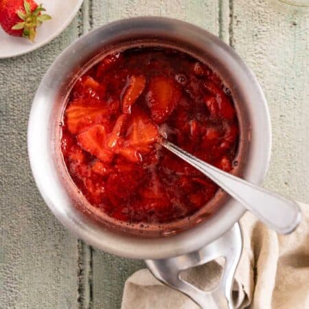 Strawberry compote in a stainless steel pot with a spoon in it.