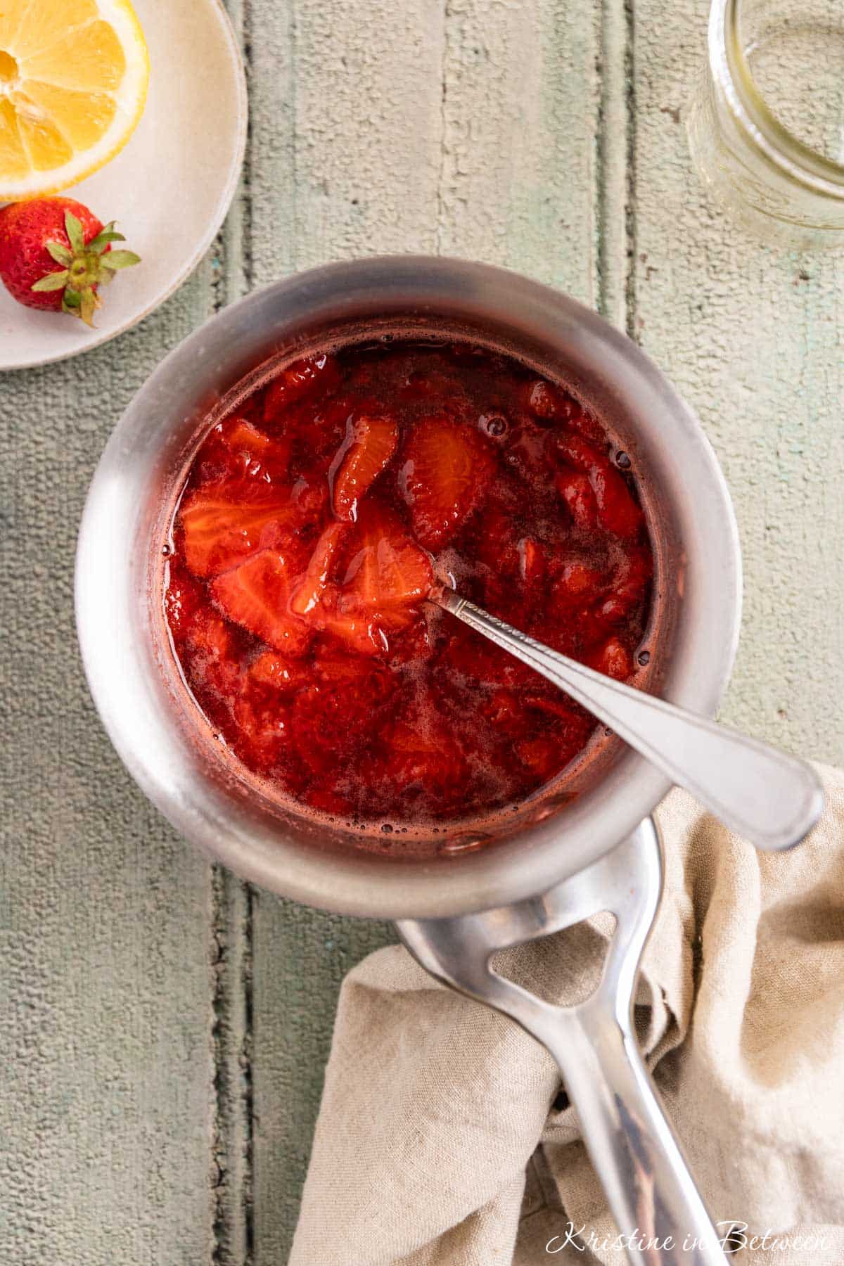 Strawberry compote in a stainless steel pot with a spoon in it.