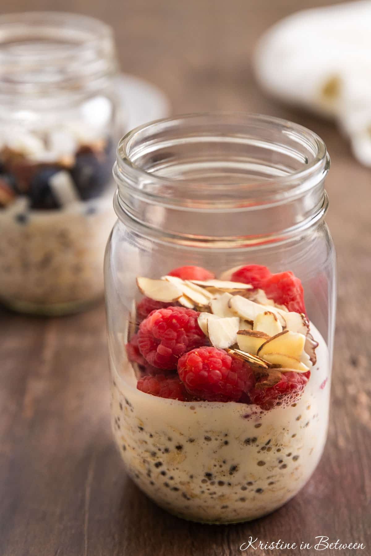A mason jar of vanilla overnight oats topped with raspberries and almonds.
