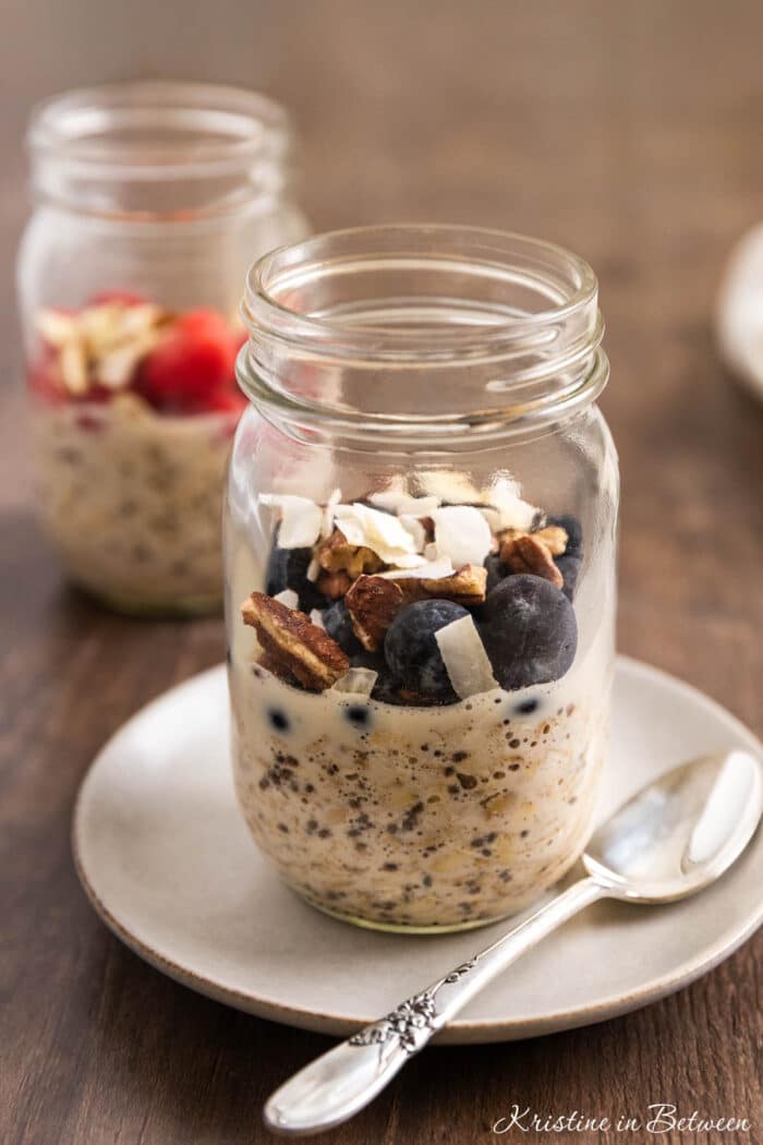 Overnight oats in a glass jar topped with blueberries, pecans, and coconut.