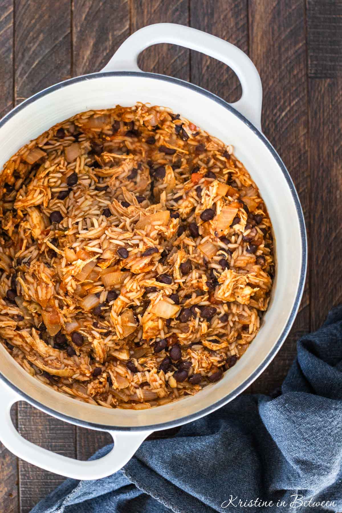 A white Dutch oven filled with chicken taco casserole with a wooden spoon next to it.