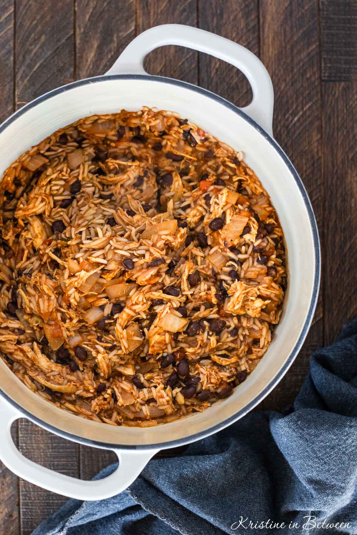 A white Dutch oven filled with chicken taco casserole with a wooden spoon next to it.