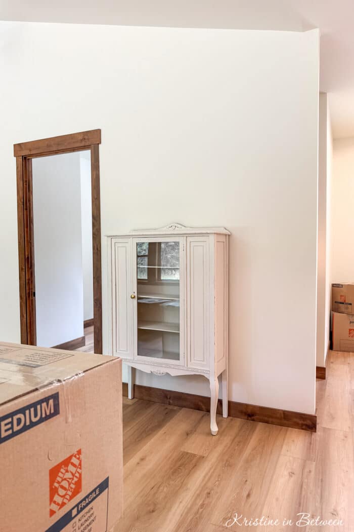 An antique china cabinet sitting in an empty house with moving boxes.