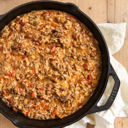 Cheesy ground beef and rice in a cast iron skillet with an antique spoon.
