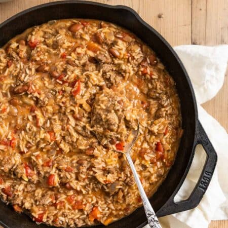 Cheesy ground beef and rice in a cast iron skillet with an antique spoon.