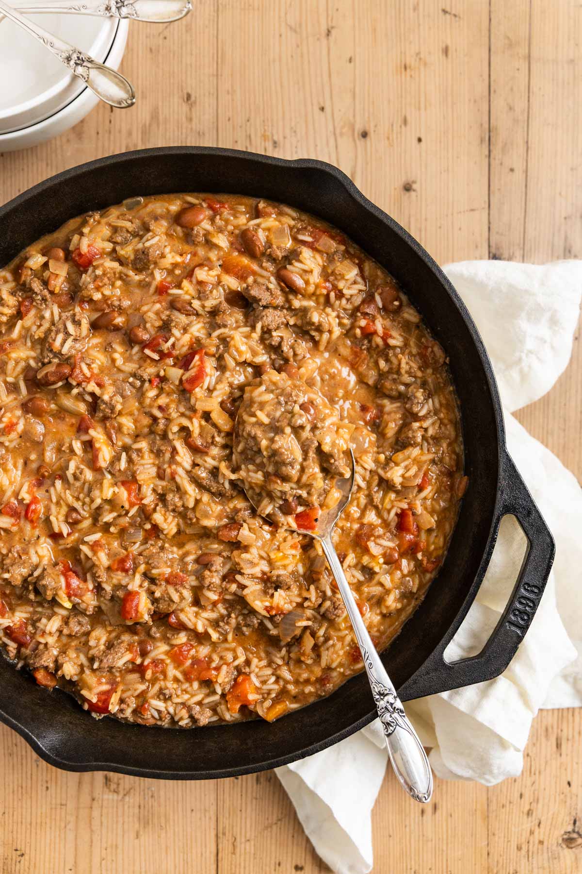 Cheesy ground beef and rice in a cast iron skillet with an antique spoon.