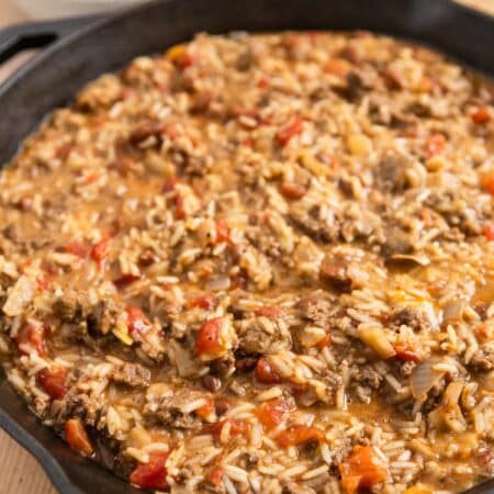 Cheesy ground beef and rice in a cast iron skillet with an antique spoon.