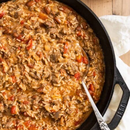 Cheesy ground beef and rice in a cast iron skillet with an antique spoon.
