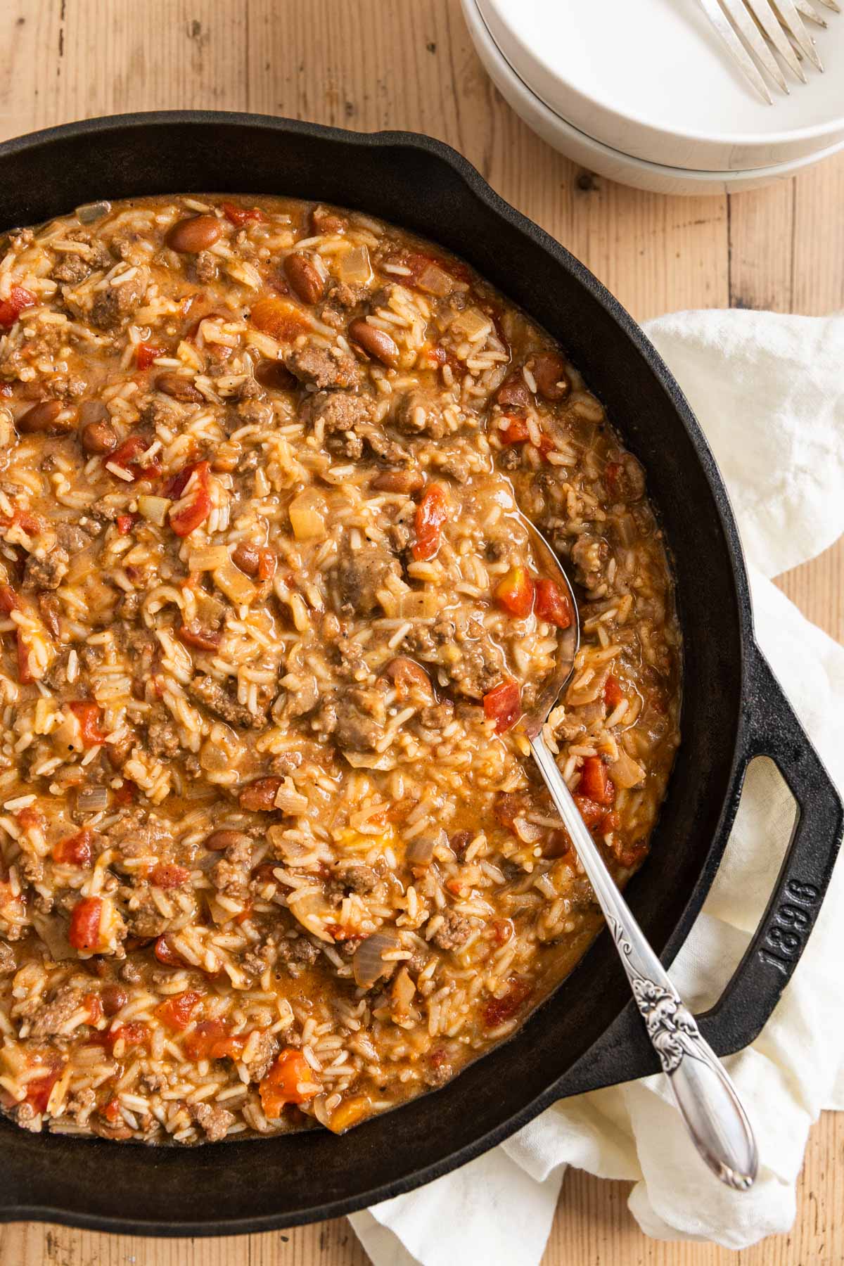 Cheesy ground beef and rice in a cast iron skillet with an antique spoon.