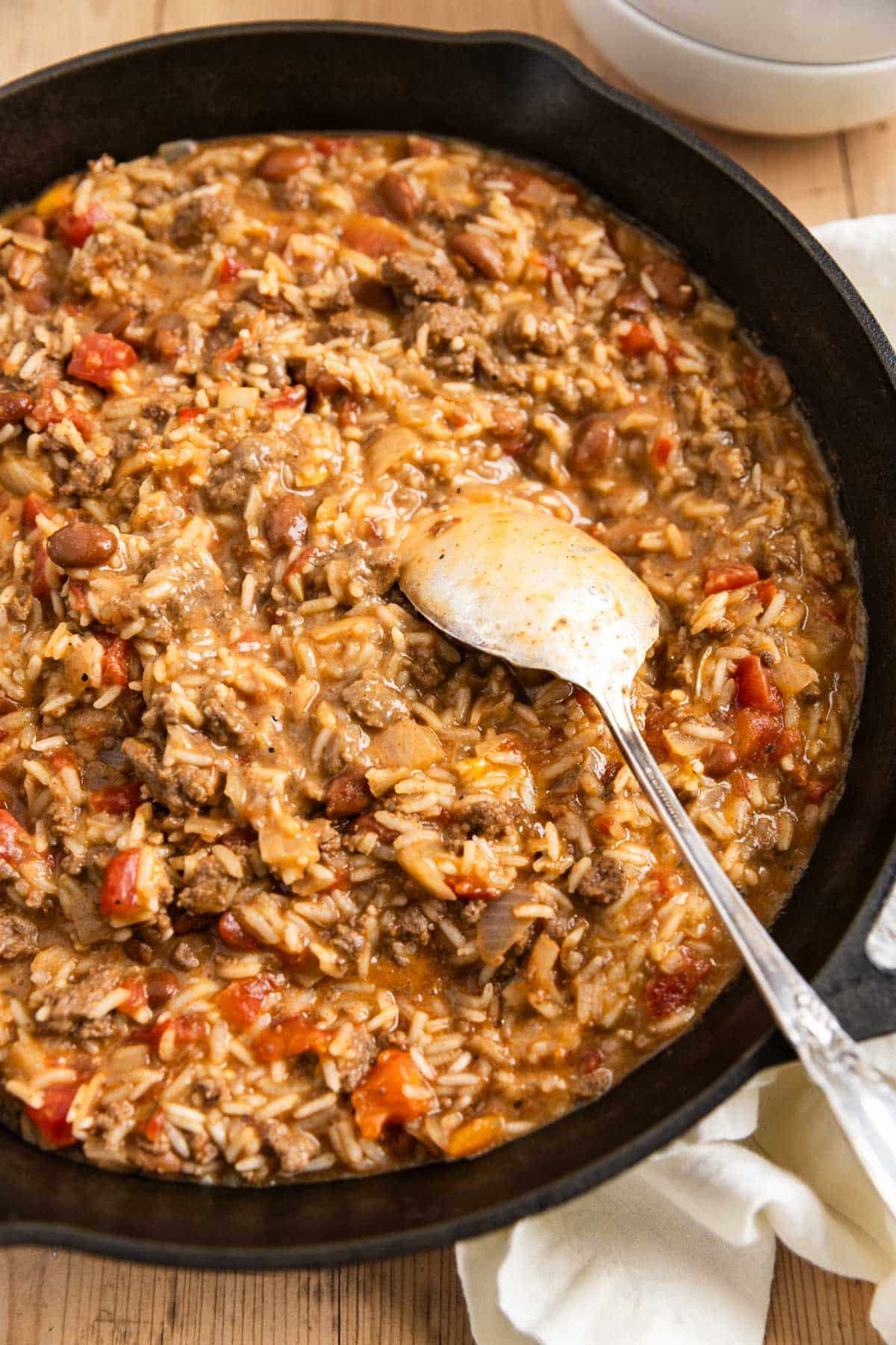 Cheesy ground beef and rice in a cast iron skillet with an antique spoon.