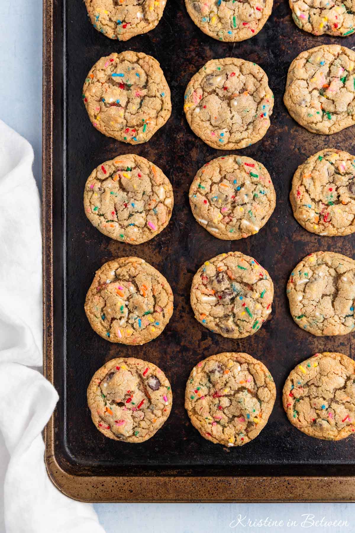 A whole batch of cookies laying on an old cookie sheet with a white napkin next to it.