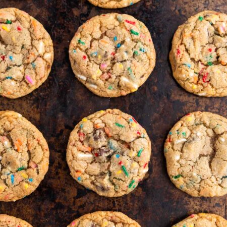 A whole batch of cookies laying on an old cookie sheet with a white napkin next to it.