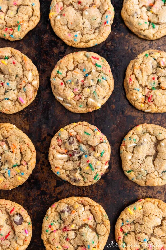 A whole batch of cookies laying on an old cookie sheet with a white napkin next to it.