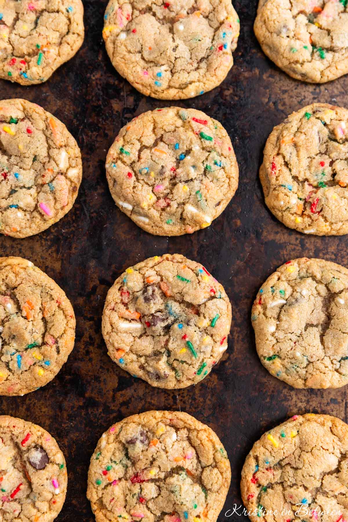 A whole batch of cookies laying on an old cookie sheet with a white napkin next to it.