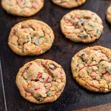 A whole batch of cookies laying on an old cookie sheet with a white napkin next to it.