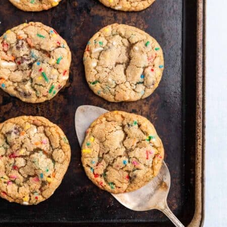 A whole batch of cookies laying on an old cookie sheet with a white napkin next to it.