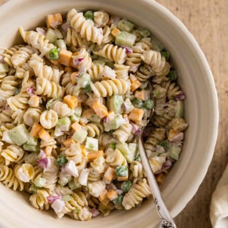 A large bowl of pasta salad with cheese and peas and a spoon stuck in it.