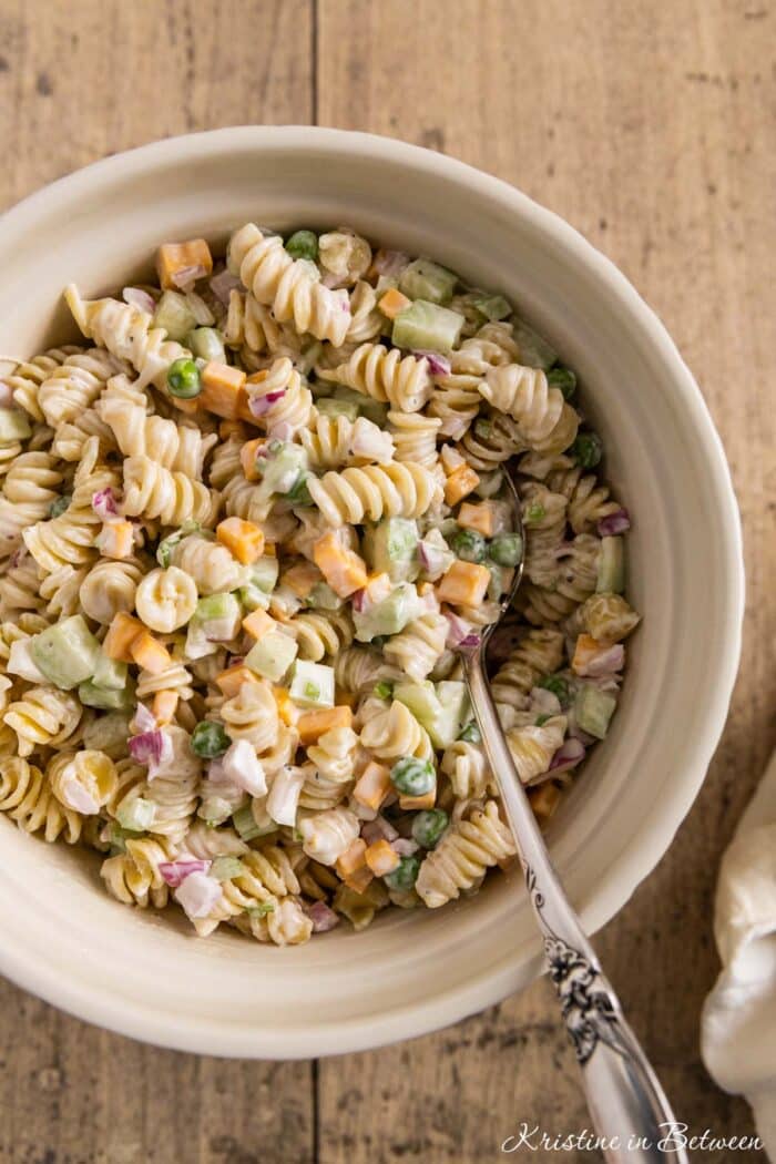 A large bowl of pasta salad with cheese and peas and a spoon stuck in it.
