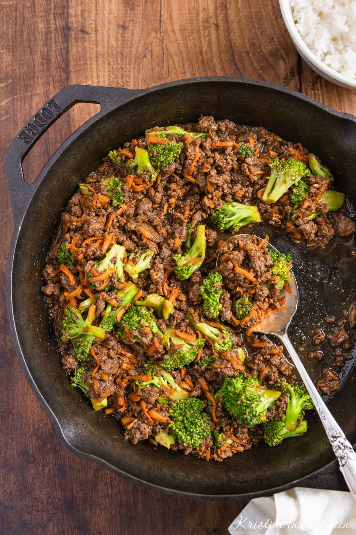 Ground beef teriyaki with broccoli and carrots in a cast iron skillet with an antique spoon.