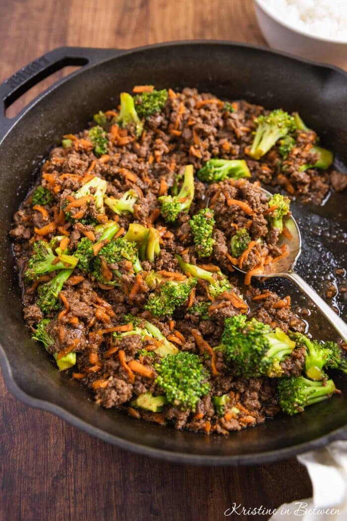 Ground beef teriyaki with broccoli and carrots in a cast iron skillet with an antique spoon.