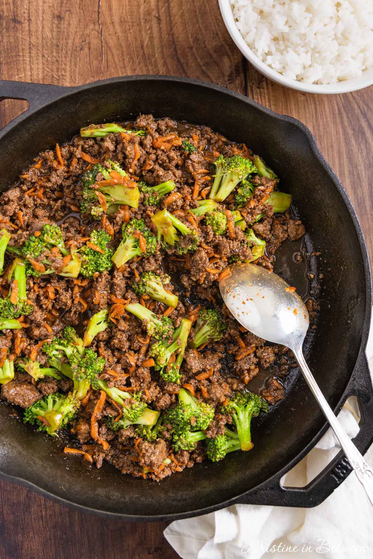 Ground beef teriyaki with broccoli and carrots in a cast iron skillet with an antique spoon.