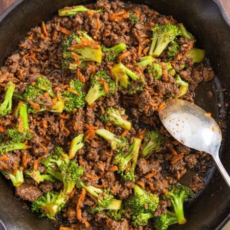 Ground beef teriyaki with broccoli and carrots in a cast iron skillet with an antique spoon.
