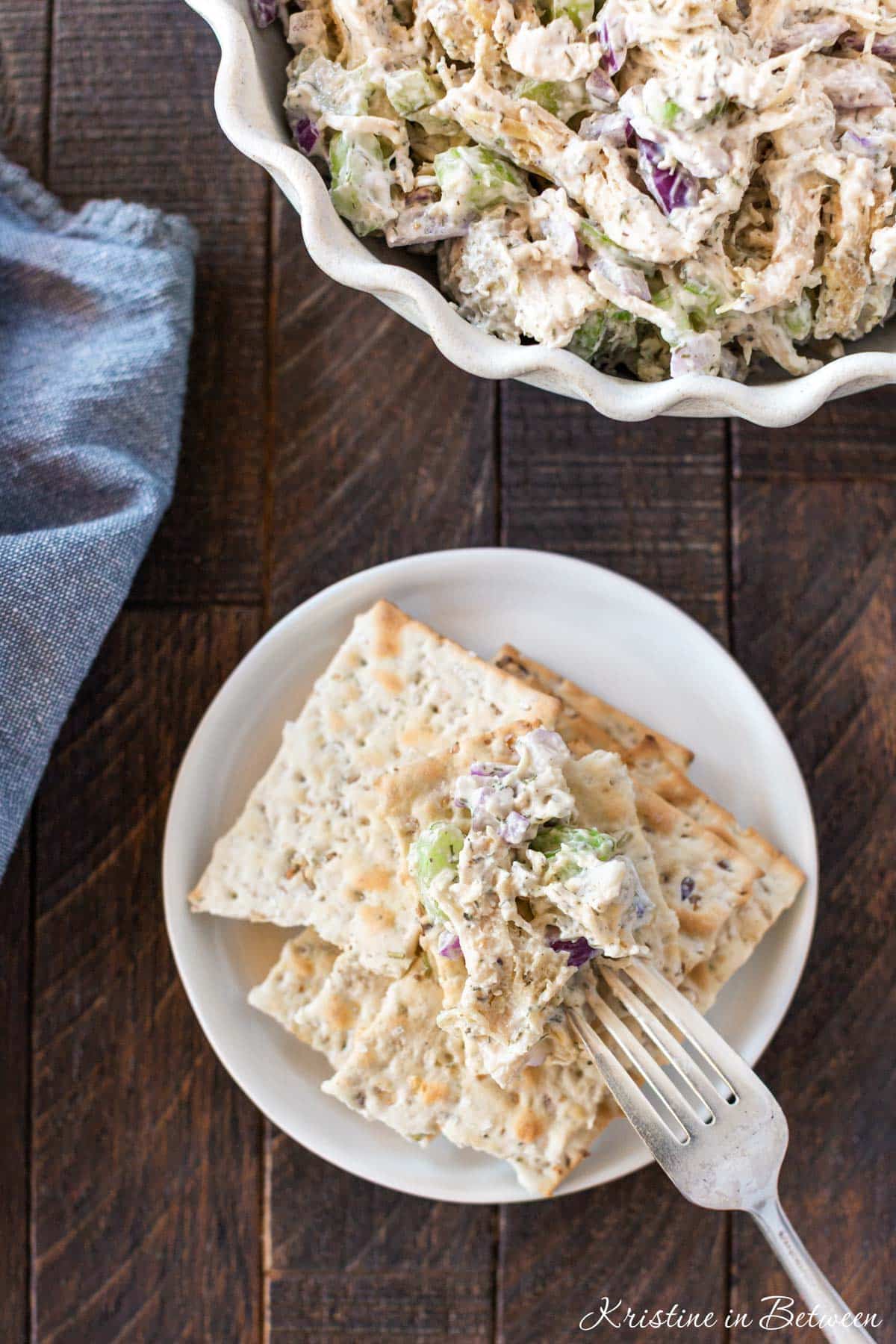 Crackers on a white plate with a bite of chicken salad on top and a fork laying next to them.