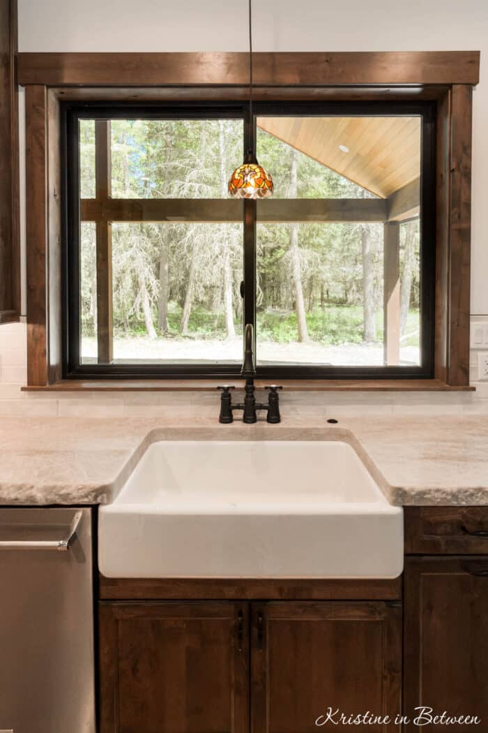 A fancy pendant hanging over a farmhouse sink in front of a window with a view of pine trees.