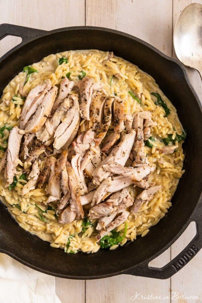 Lemon chicken orzo in a cast iron skillet with a spoon next to it.