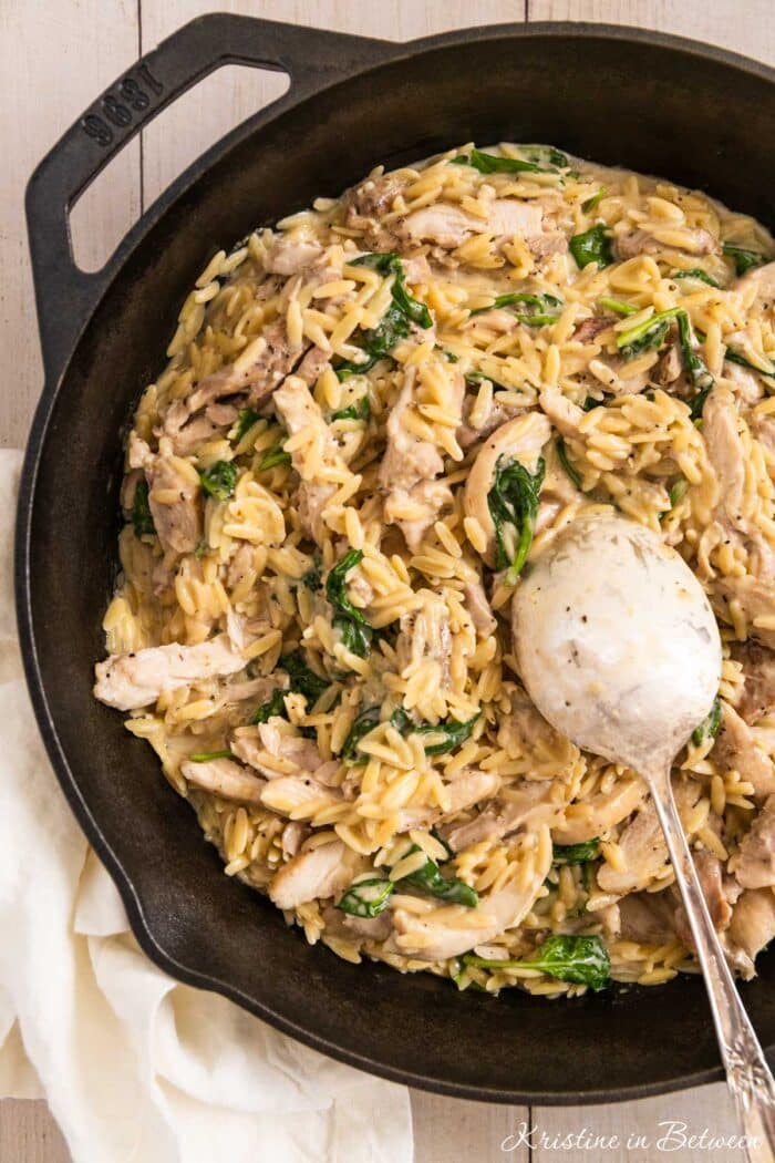 Lemon chicken orzo in a cast iron skillet with a spoon in it, ready to serve.