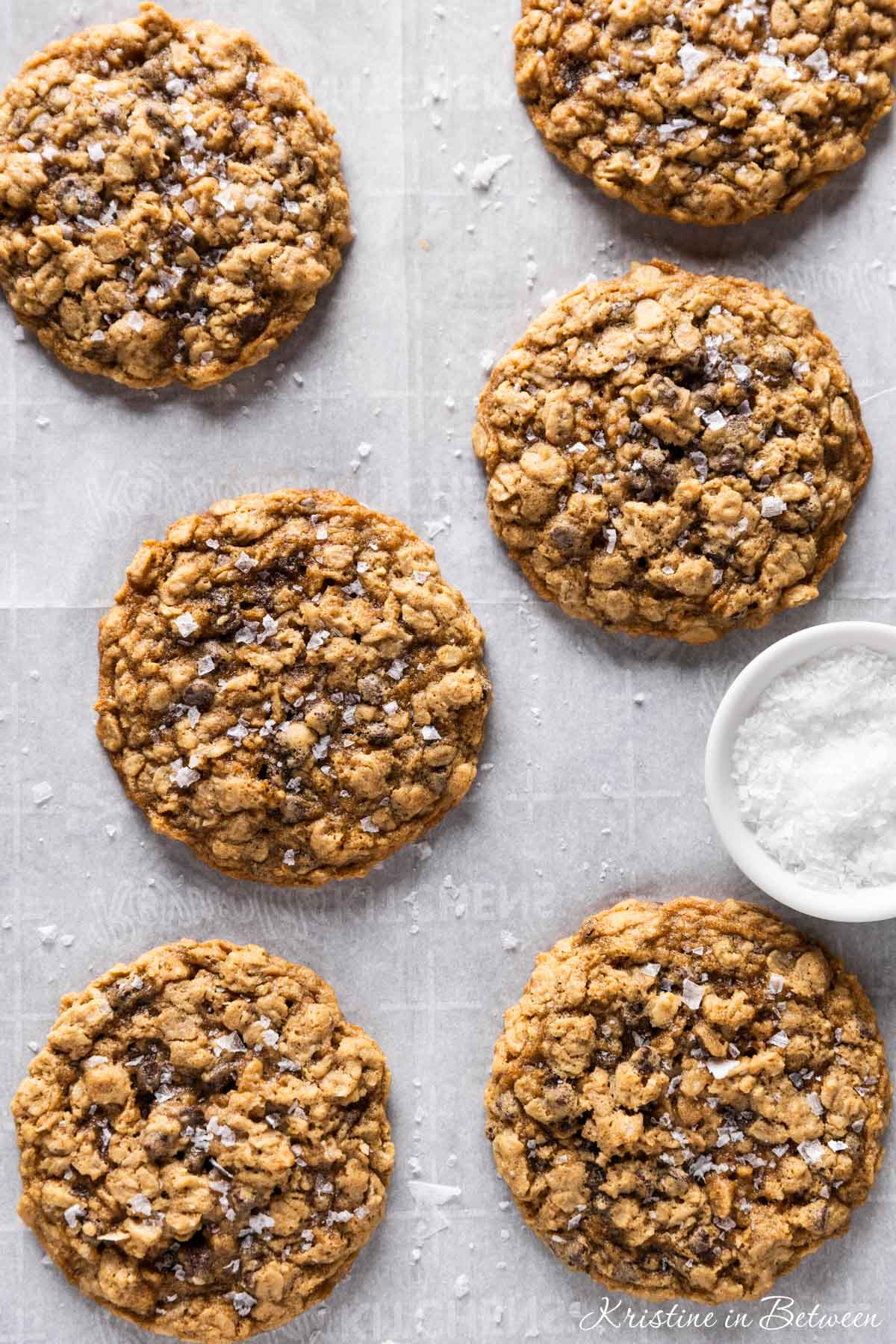 Oatmeal dark chocolate chunk cookies sitting on an antique baking tray with a small bowl of salt next to them.