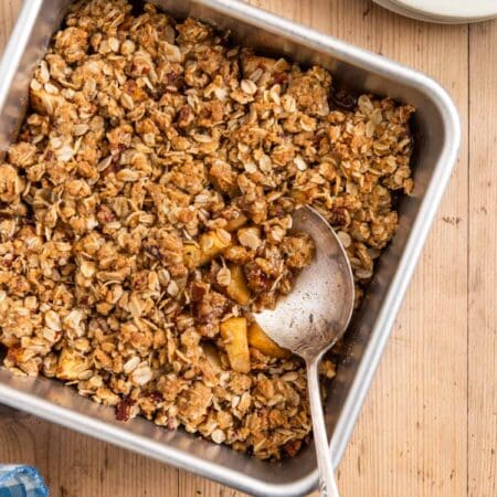 Baked apple crisp in an aluminum baking dish with a spoon in it.