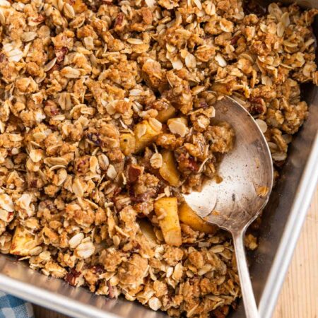 Baked apple crisp in an aluminum baking dish with a spoon in it.