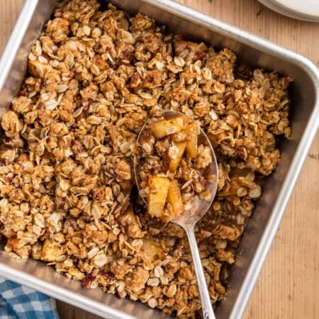 Baked apple crisp in an aluminum baking dish with a spoon in it.
