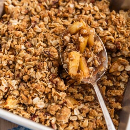 Baked apple crisp in an aluminum baking dish with a spoon in it.