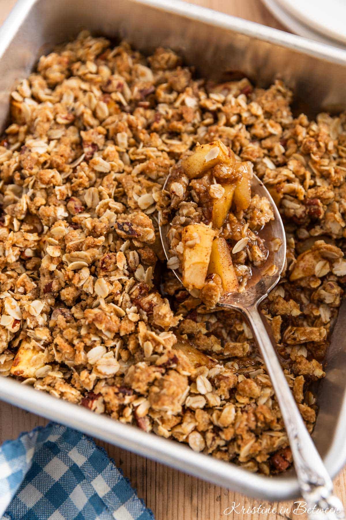 Baked apple crisp in an aluminum baking dish with a spoon in it.