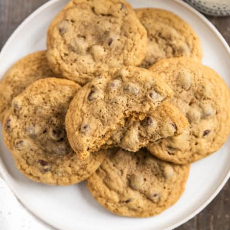 Chocolate chip cookies laying on a white plate with an eyelet napkin and a glass of milk in the background.