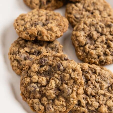 Oatmeal chocolate chip cookies stacked up on a white platter.