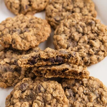 Oatmeal chocolate chip cookies stacked up on a white platter with a glass of milk in the background.