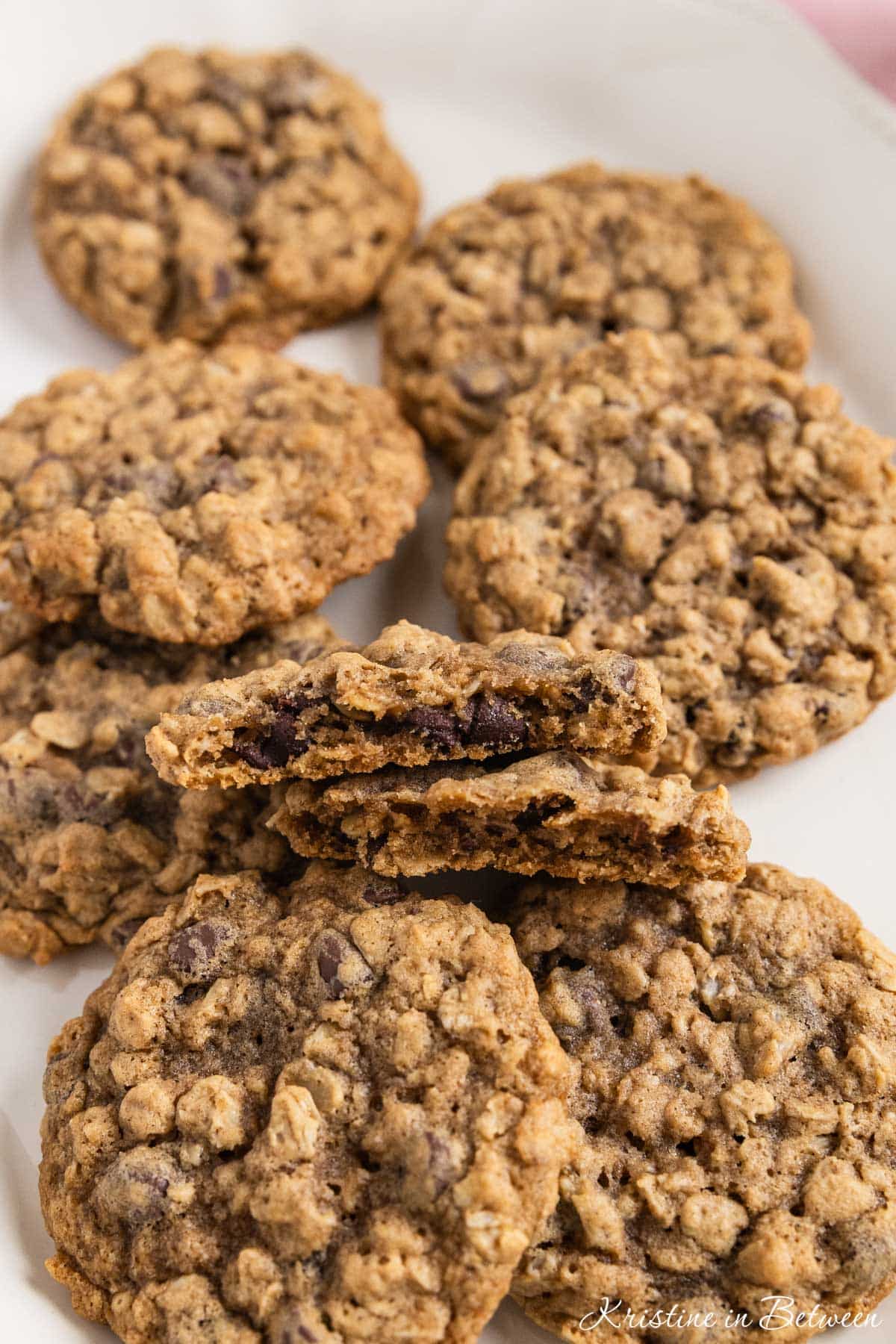 Oatmeal chocolate chip cookies stacked up on a white platter with a glass of milk in the background.