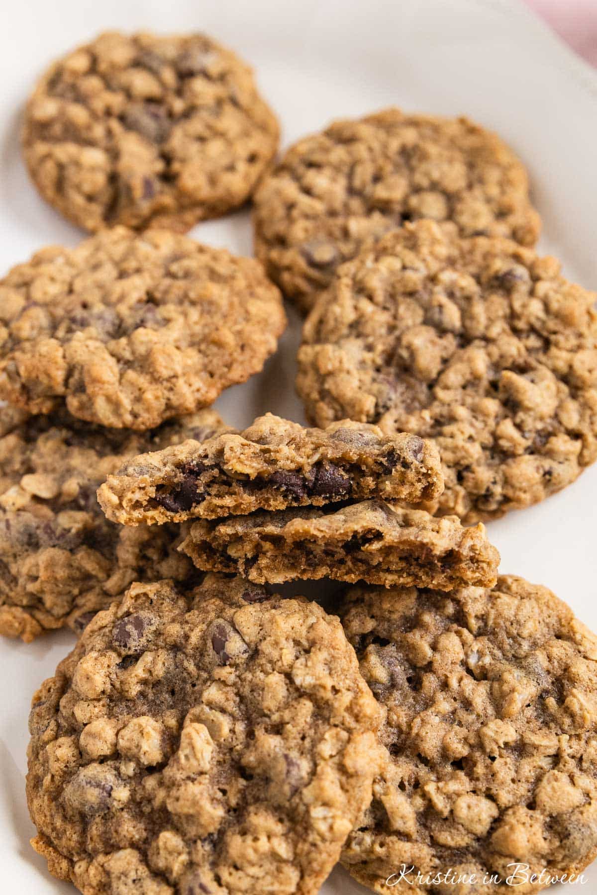 Oatmeal chocolate chip cookies stacked up on a white platter with a glass of milk in the background.