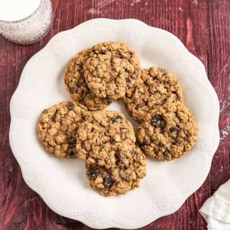 Old-fashioned oatmeal raisin cookies stacked upon a white plate with one broken in half to show the inside.