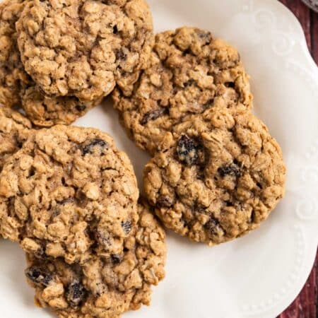 Old-fashioned oatmeal raisin cookies stacked upon a white plate with one broken in half to show the inside.